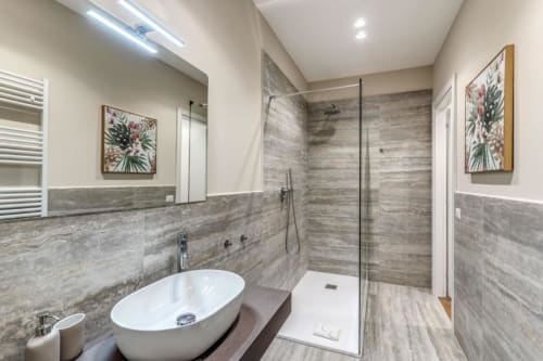 Bagno moderno in appartamento romano con doccia in legno-piastrelle grigie, lavabo ovale bianco e quadri decorativi floreali