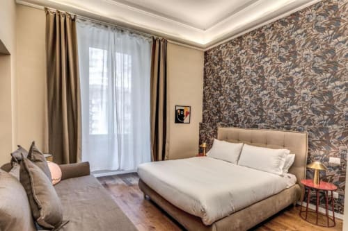 Camera moderna dell'appartamento Downtown Srl Roma con letto beige, carta da parati decorativa, balcone con vista sulla città e design elegante