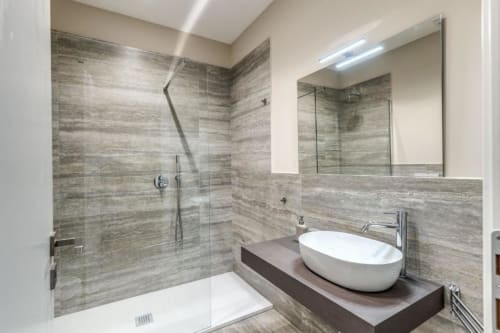 Bagno moderno nell'appartamento Downtown Srl Roma con doccia in piastrelle grigie, lavabo bianco e specchio illuminato