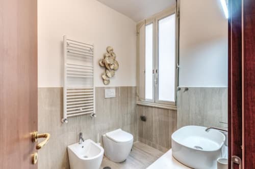 Bagno moderno in appartamento romano con wc, bidet, lavabo da appoggio, scaldasalviette e finiture in legno-ceramica