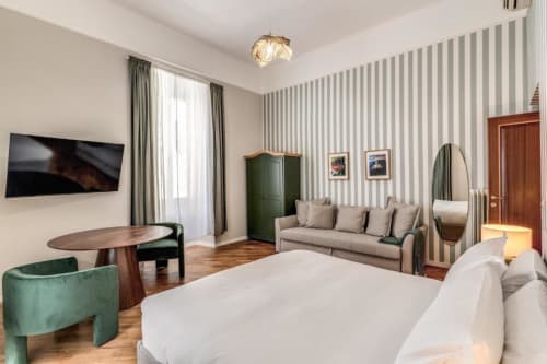 Camera da letto di moderno appartamento a Roma con divano grigio, carta da parati a righe, mobili in legno e TV a schermo piatto presso Downtown Srl