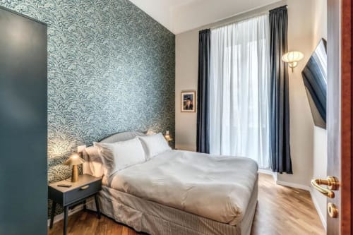 Camera da letto moderna con carta da parati turchese a motivi, biancheria bianca, pavimenti in legno all'apartamento Downtown Roma