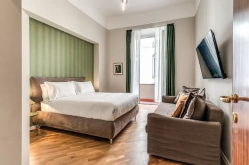 Moderno monolocale a Roma con letto matrimoniale, parete a righe verdi, TV a muro, divano marrone e parquet