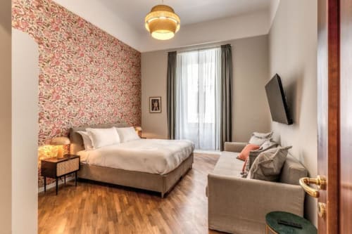 Camera da letto moderna a Roma con carta da parati floreale rosa, letto matrimoniale, parquet, zona salotto e TV a parete
