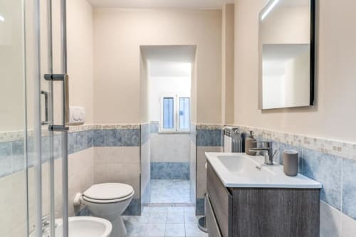 Bagno moderno con dettagli in piastrelle azzurre, lavabo, wc, specchio e doccia nell'appartamento Downtown Nobu, Roma