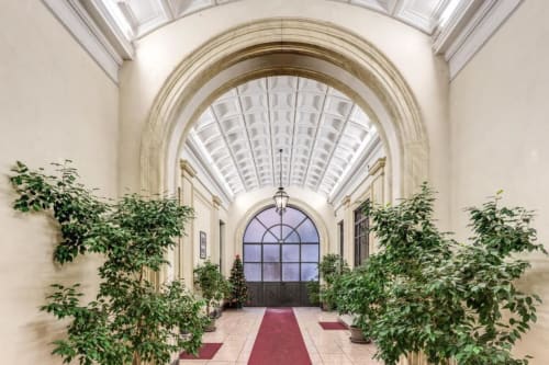 Elegante corridoio ad archi nel Downtown Roma apartment con soffitto in vetro, piante e tappeto rosso che conduce all'ingresso