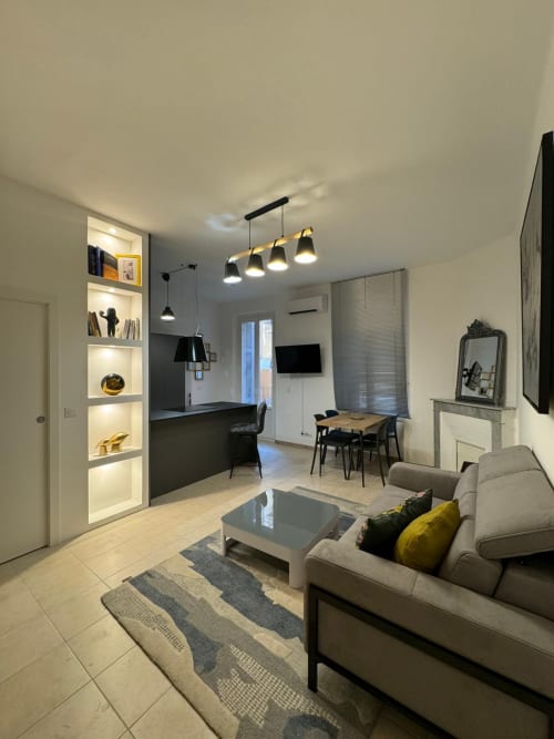 Spacieux salon d'appartement moderne à Bastia avec canapé beige, table à manger, cuisine ouverte et étagères illuminées