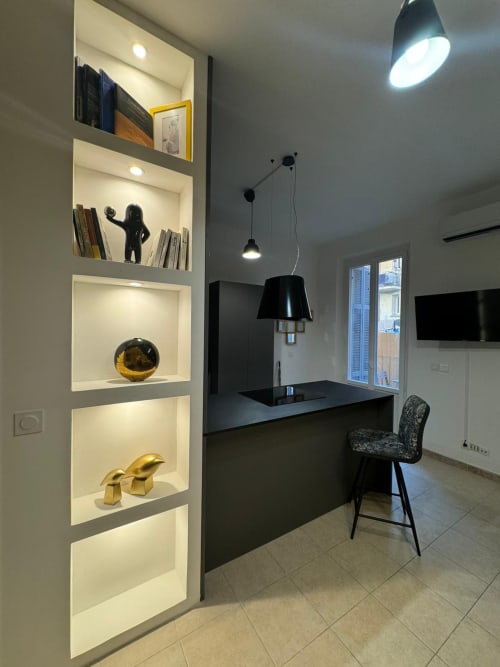 Espace de travail moderne à Bastia avec étagères lumineuses, bureau noir, luminaires suspendus et portes vitrées ouvertes sur