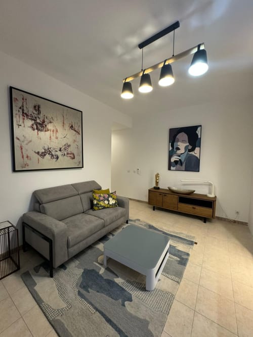 Salon moderne avec canapé gris, table basse blanche, luminaires suspendus et œuvres murales à l'appartement Altezza, Bastia