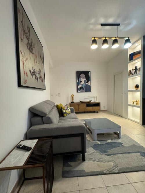 Salon moderne dans un appartement de Bastia avec canapé gris, mobilier en bois, suspensions et œuvres d'art encadrées