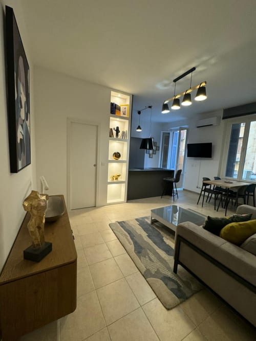 Salon moderne d'un appartement à Bastia avec canapé, coin repas, kitchenette et luminaires contemporains