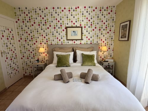 Chambre double aux Vieilles Digues avec papier peint à motifs, oreillers verts et vue sur le jardin