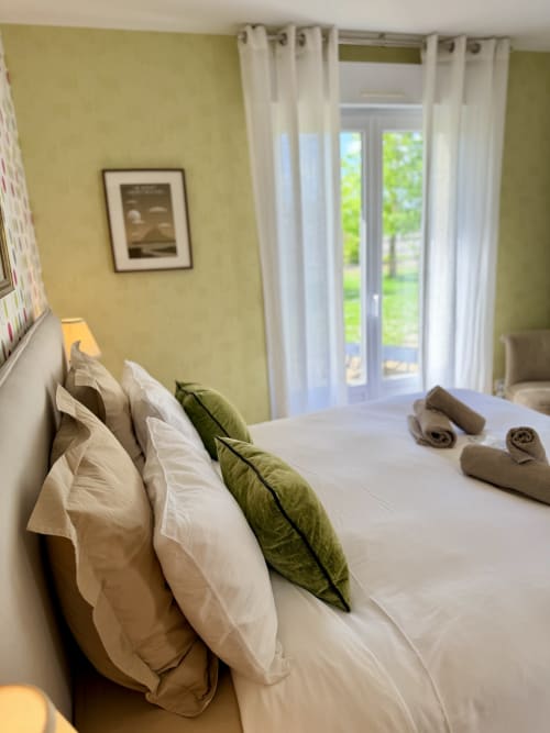 Belle chambre double aux murs jaunes, oreillers blancs, coussin vert et vue sur le jardin aux Vieilles Digues