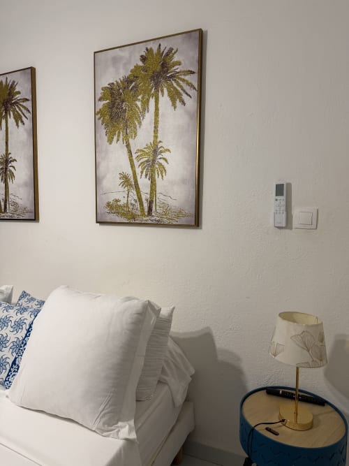Chambre à Kaz Kafe BnB avec literie blanche, oreiller motifs bleus, tableau de palmiers, lampe de chevet et climatiseur