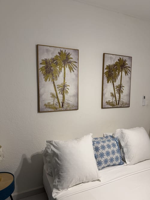 Chambre avec oreillers blancs et coussin bleu à motifs, deux cadres de palmiers au-dessus du lit au Kaz Kafe à Mamoudzou
