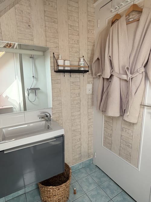 Salle de bains moderne aux Vieilles Digues à Beauvoir avec carrelage bois, lavabo, douche et peignoirs