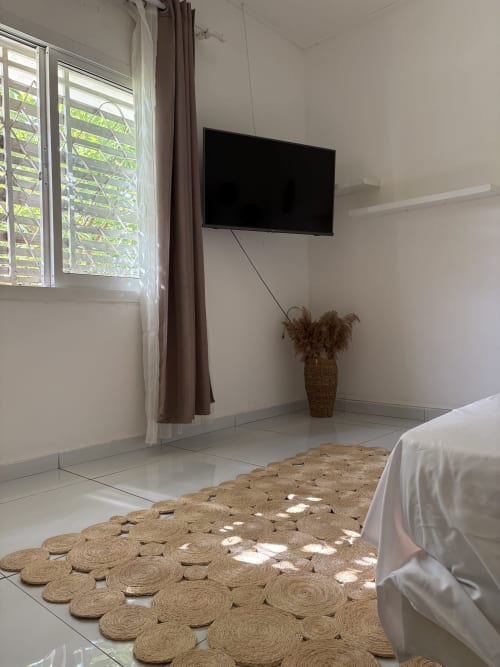 Chambre épurée à Kaz Kafe BnB avec tapis ronds tissés, lit blanc, TV murale et vue sur le jardin