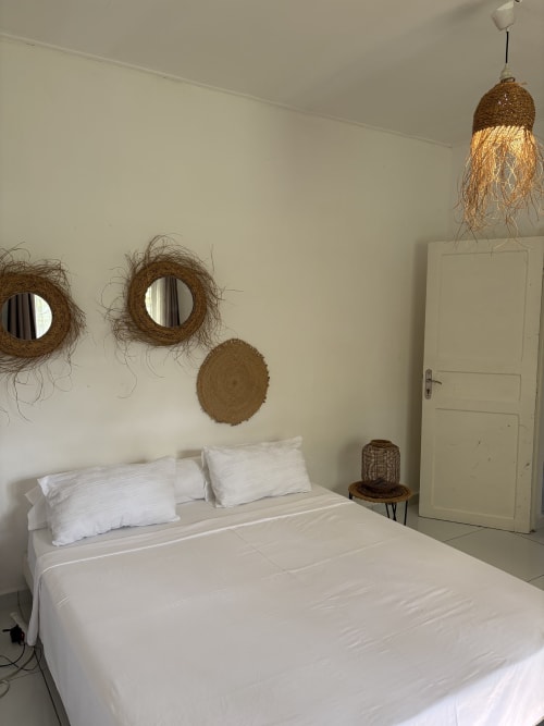 Chambre lumineuse au Kaz Kafe à Mamoudzou avec lit blanc, miroirs tressés et décoration naturelle