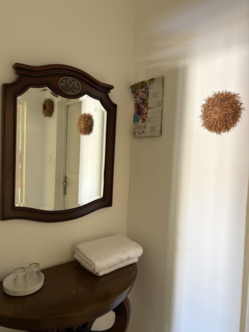 Vasque de salle de bain avec miroir en bois sombre, serviettes blanches et décoration murale tressée au Kaz Kafe à Mamoudzou
