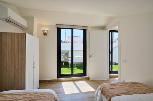 Moderno dormitorio en apartamento Tr3sor 31, Calella, con camas gemelas y puertas negras que abren a terraza jardín