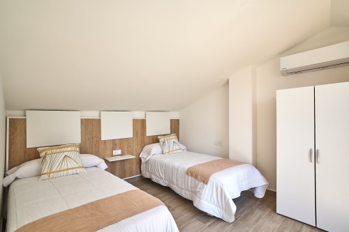 Habitación doble en apartamento Tr3sor Homes, Calella, con ropa de cama blanca, cabeceros de madera y mobiliario moderno