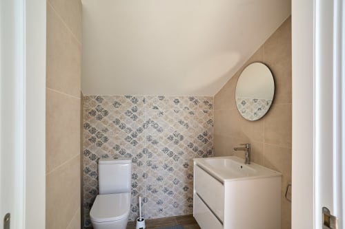Baño moderno del apartamento Tr3sor 31 en Calella con lavamanos blanco, inodoro, azulejos estampados y espejo redondo