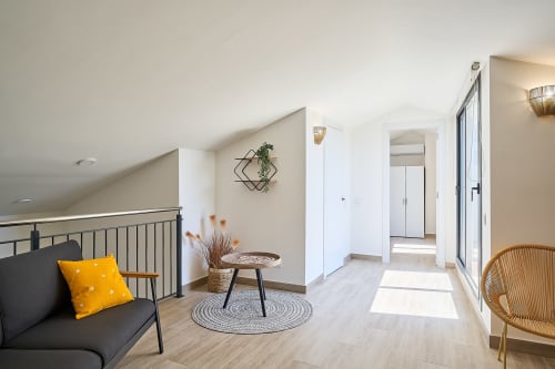 Elegante salón entresuelo en apartamento Tr3sor Homes, Calella, con asientos, mesa redonda y luz natural desde balcón.