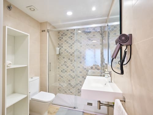 Baño moderno en apartamento Tr3sor 31 en Calella con ducha de acceso directo, lavamanos blanco, inodoro y toallero climatizado