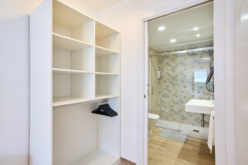 Moderno walk-in closet y baño con estanterías blancas y ducha de cristal en el apartamento Tr3sor 31 de Calella