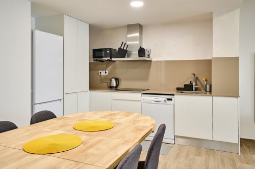 Moderna zona de comedor en apartamento Tr3sor 31, Calella, con mesa de madera, individuales amarillos, muebles blancos y