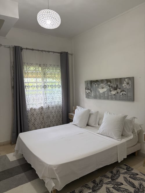 Chambre Zen Bambou de Kaz Kafe BnB à Mamoudzou avec lit blanc, lustre en cristal et vue sur jardin