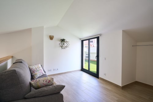 Moderno apartamento dúplex en Calella con salón abierto, sofá gris y puertas de cristal hacia terraza jardín
