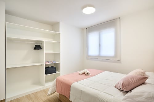 Dormitorio moderno en Tr3sor Homes, Calella, con cama, ropa de cama rosa, estanterías blancas y luz natural