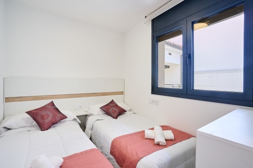 Dormitorio moderno en Tr3sor Homes, Calella, con camas gemelas, detalles en borgoña y ventana con marco azul