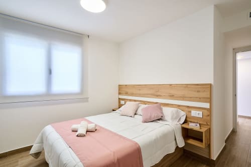 Moderno dormitorio en Tr3sor 32 Delux Duplex de Tr3sor Homes Calella con cabecero de madera, ropa de cama rosa y luz natural