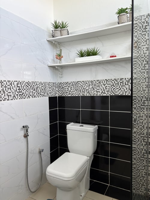 Salle de bain moderne de la chambre Zen Bambou chez Kaz Kafe : marbre blanc, touches noires, étagères flottantes et plantes en pots