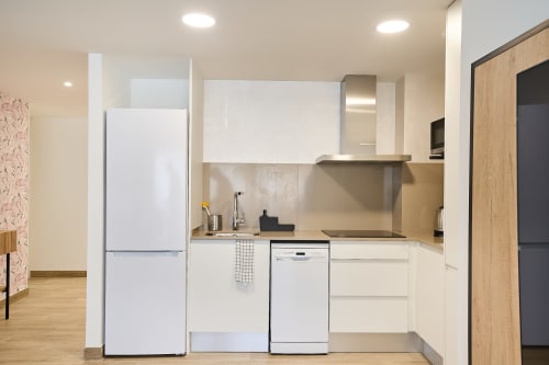 Cocina moderna en apartamento dúplex de lujo Tr3sor Homes, Calella, con gabinetes blancos y electrodomésticos de acero inoxidable