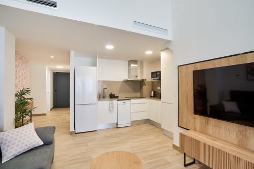 Amplia sala de estar abierta en Tr3sor 32 Delux Duplex, Calella, con cocina blanca, suelos de madera, TV y diseño contemporáneo