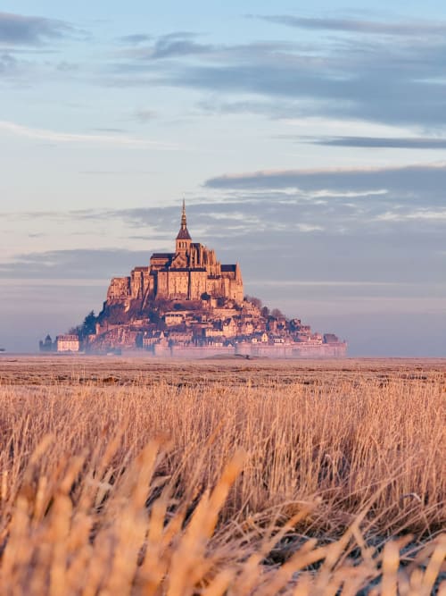 El castillo de Mont-Saint-Michel al atardecer dominando los campos dorados cerca de Les Vieilles Digues, Beauvoir, Francia