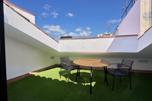 Soleada terraza en la azotea de Tr3sor 33 en Calella con mesa de madera, sillas negras y césped artificial