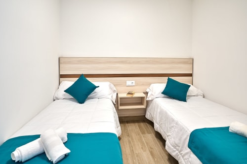 Habitación doble con acentos turquesas en Tr3sor Homes, Calella. Dos camas individuales con sábanas blancas y almohadas turquesas.