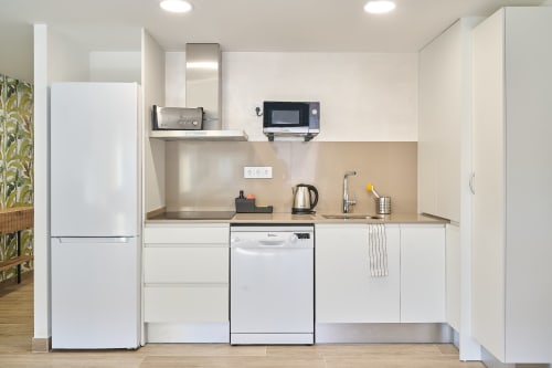 Cocina moderna blanca en apartamento Tr3sor Homes, Calella, España con electrodomésticos y encimera de acero inoxidable