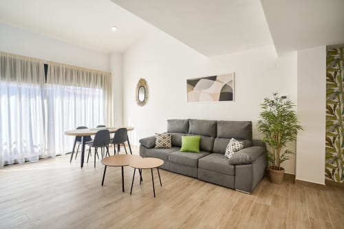 Sala de estar moderna en apartamento dúplex Tr3sor 33, Calella, con sofá gris, comedor y acceso a balcón