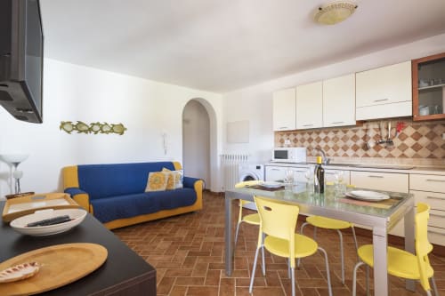 Cucina e zona pranzo moderne a Youinsardinia a Bari Sardo con divano blu, sedie gialle e piastrelle geometriche