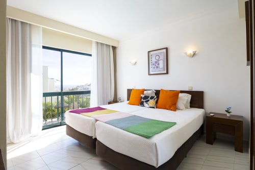 Quarto moderno e luminoso na RB Algarve com camas de solteiro, almofadas laranja, varanda com vista para a piscina e móveis contemporâneos