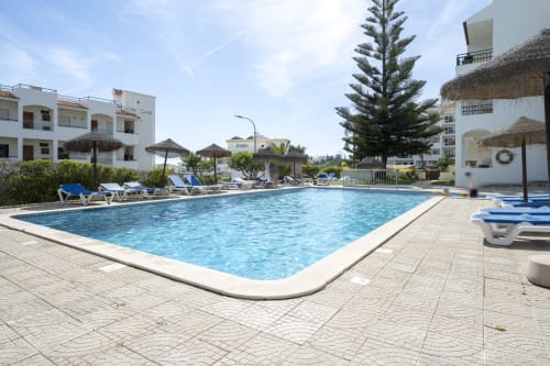 Área de piscina do RB Algarve em Albufeira com espreguiçadeiras, guarda-sóis e edifícios de apartamentos brancos próximos