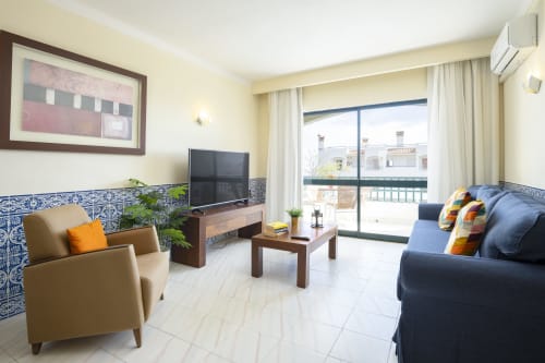 Sala moderna do apartamento RB Algarve Albufeira com poltrona bege, sofá azul, TV e vista da varanda