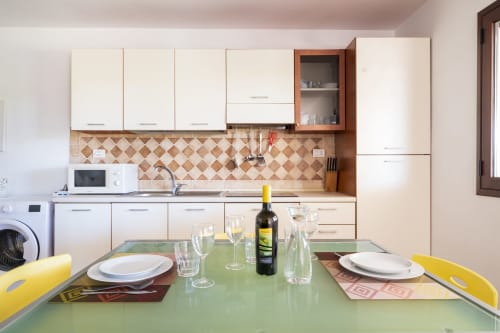 Cucina e zona pranzo moderna di Youinsardinia a Bari Sardo con tavolo verde, bottiglia di vino e coperto