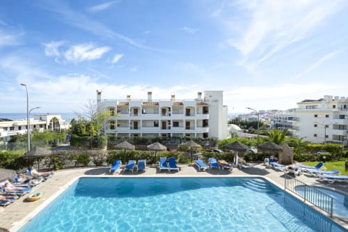 Piscina do RB Algarve com espreguiçadeiras azuis, edifício branco de apartamentos e vista para o mar em Albufeira, Portugal
