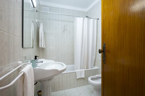 Banheiro moderno do apartamento RB Algarve com pia branca, vaso sanitário e chuveiro com cortina em Albufeira, Portugal